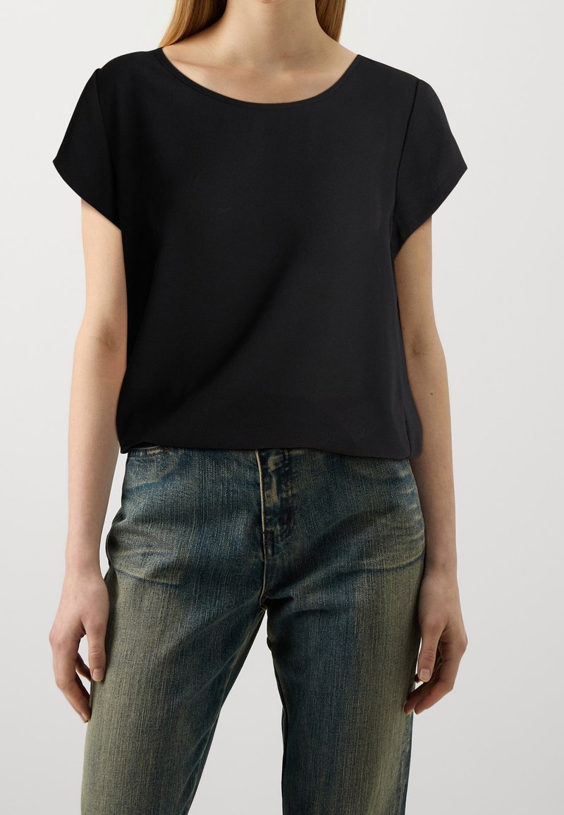 Top nero a maniche corte con scollatura rotonda, realizzato in un tessuto liscio, abbinato a jeans blu leggermente sbiaditi a vita alta.