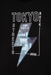 Black t-shirt featuring a white lightning bolt graphic. Text reads “TOKYO,” “STREETS,” and “JAPAN” with an urban scene inside the bolt.