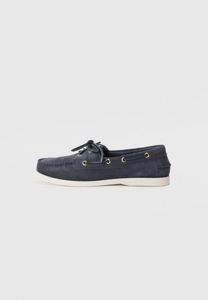 Navy blue suede boat shoe with a rounded toe, white rubber sole, and gold eyelets. Features a lace-up closure with matching laces.