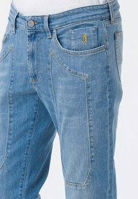 Jeans in denim azzurro chiaro con una vestibilità leggermente affusolata, caratterizzati da ampie tasche anteriori, cuciture discrete e un piccolo logo ricamato sulla tasca.