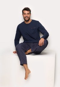 Marineblå langærmet top med en brystlomme og bordeaux stribede pyjamabukser, der har en afslappet pasform og blødt bomuldsstof.