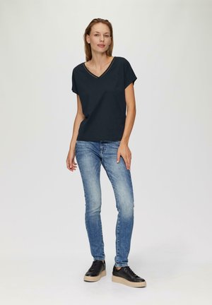 Marinefarbener V-Ausschnitt-T-Shirt mit kurzen Ärmeln, kombiniert mit hellblauen Skinny-Jeans und schwarzen Sneakers mit einer dicken beigen Sohle. Glatte Stofftextur.