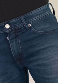 Jeans in denim blu scuro con una texture liscia, design classico a cinque tasche, chiusura con bottone in metallo e dettagli di cucitura sottili.