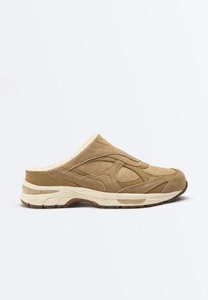 Mule sneaker marron clair à enfiler avec doublure en polaire beige, tige en daim, et semelle épaisse en caoutchouc avec crampons pour une utilisation en extérieur.