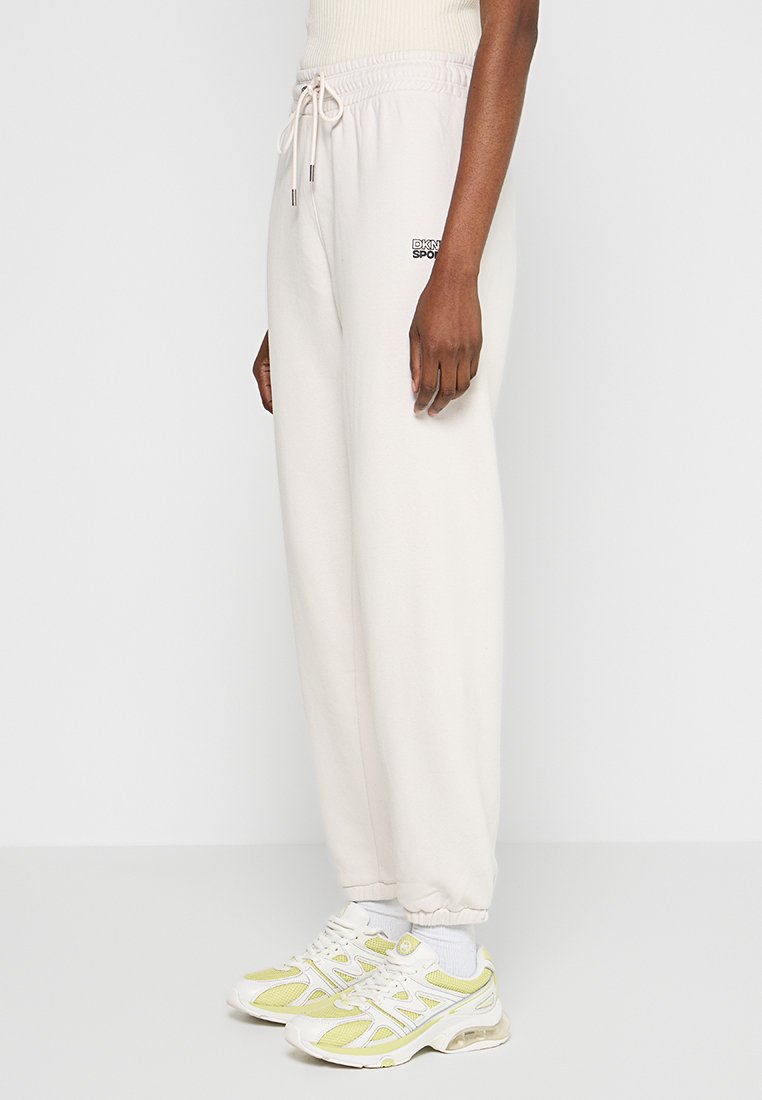 Jasnobeżowe spodnie dresowe wykonane z miękkiej bawełny, z elastycznym pasem w talii i sznurkiem, oraz małym logo na biodrze.