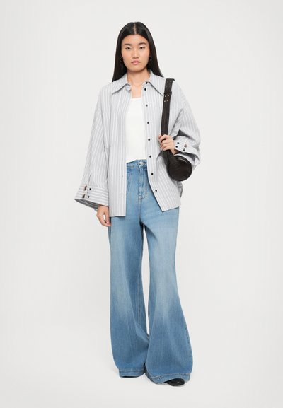 Striped oversized gray shirt with buttons, white tank top, high-waisted wide-leg denim jeans, and a small black handbag.