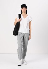 Vit V-ringad t-shirt, randiga grå byxor, svart keps och en svart väska. Vita sneakers fulländar den avslappnade outfiten. Enkelt mönster och neutrala färger.