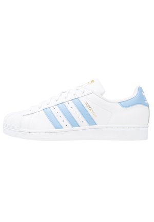 Hvid Adidas Superstar sneaker med lyseblå striber, gyldent "Superstar" tekst, skaldetå og blå hælflap med Adidas-logo.