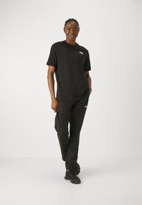 Zwarte katoenen t-shirt gecombineerd met bijpassende broek, beide met een klein logo-detail. De outfit heeft een relaxte pasvorm en een eenvoudig design.