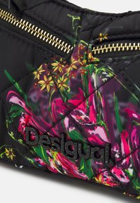 Černá prošívaná látka s barevným květinovým potiskem, dva zlaté zipy a černé vyvýšené logo "Desigual" na části tašky.