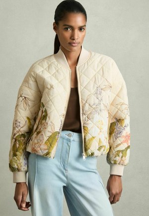 Quilted bomber jacket in light beige with floral prints in green, pink, and purple. Features a zip closure and ribbed cuffs. Tapered fit.