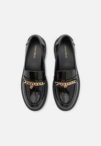 Sorte patentlæder loafers med en guldkæde-accent fragtet over forsiden, med rund tå og flad gummisål.