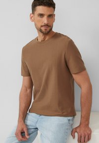 Braun gestreifte Kurzarm-T-Shirt aus weichem Stoff, mit Rundhalsausschnitt, kombiniert mit hellblauen Jeans vor einem neutralen Hintergrund.