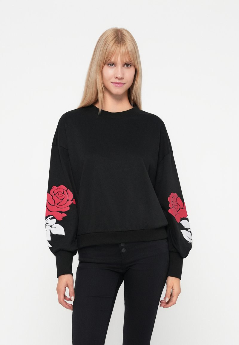 Sudadera negra con mangas largas y abullonadas que presenta estampados de rosas rojas y blancas en la manga izquierda. Diseñada para un ajuste relajado.
