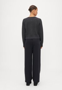 Grå stickad tröja med cropped passform och ribbat nederdel, tillsammans med högmidjade svarta vida byxor. Strukturerad tyg synlig på tröjan.