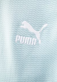Tissu texturé bleu clair avec un logo Puma brodé en blanc et une inscription. Design minimaliste axé sur les détails de marque sportive.