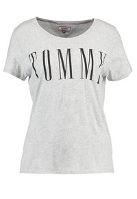 Camiseta de algodón gris, de manga corta, con cuello redondo. Presenta un estampado negro que dice "TOMMY" en una fuente moderna y en negrita en la parte frontal.