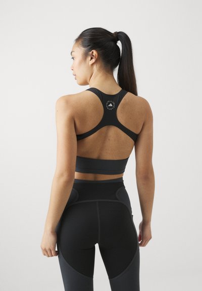 Top sportivo nero con spalline regolabili, caratterizzato da un design racerback e un dettaglio con logo. Abbinato a leggings neri a vita alta.