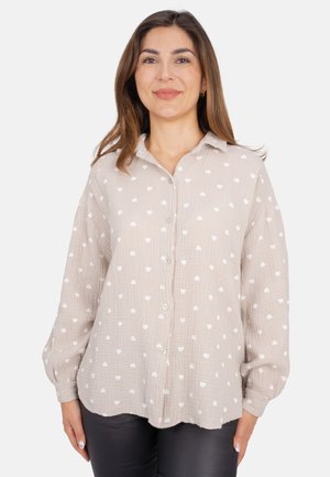 Light beige button-up shirt with white heart patterns, long sleeves, and a relaxed fit. Made of textured fabric with a collared neckline.