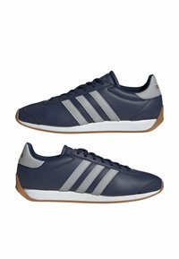 Paire de chaussures de sport bleu marine avec des rayures grises, des semelles intermédiaires blanches et des semelles extérieures en caoutchouc naturel, présentées de l'intérieur et de l'extérieur.