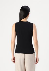 Black sleeveless top made of smooth, stretchy fabric. Features a round neckline and a fitted silhouette, paired with light beige trousers.