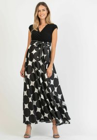 Maxi-jurk met een zwarte, getailleerde top en een vloeiende rok met grote zwart-witte cirkels. Inclusief een strik op de taille en zilveren schoenen.