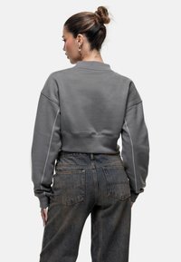 Felpa grigia cropped con maniche lunghe e dettagli in cucitura bianca, abbinata a jeans in denim scuro a vita alta, texture liscia.