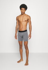 Sive športne kratke hlače s črnim pasom in logotipom Nike. Tkanina je videti gladka z minimalističnim dizajnom.