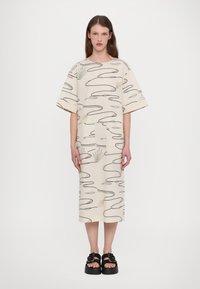 Beige mønstrete kjole med korte, brede ermer og rett snitt. Svarte abstrakte linjer og subtile plantemotiver. Kombinert med chunky svarte sandaler.
