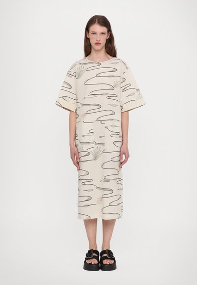 Abito beige a fantasia con maniche corte e larghe e un taglio dritto. Linee astratte nere e sottili motivi vegetali. Abbinato a sandali neri chunky.