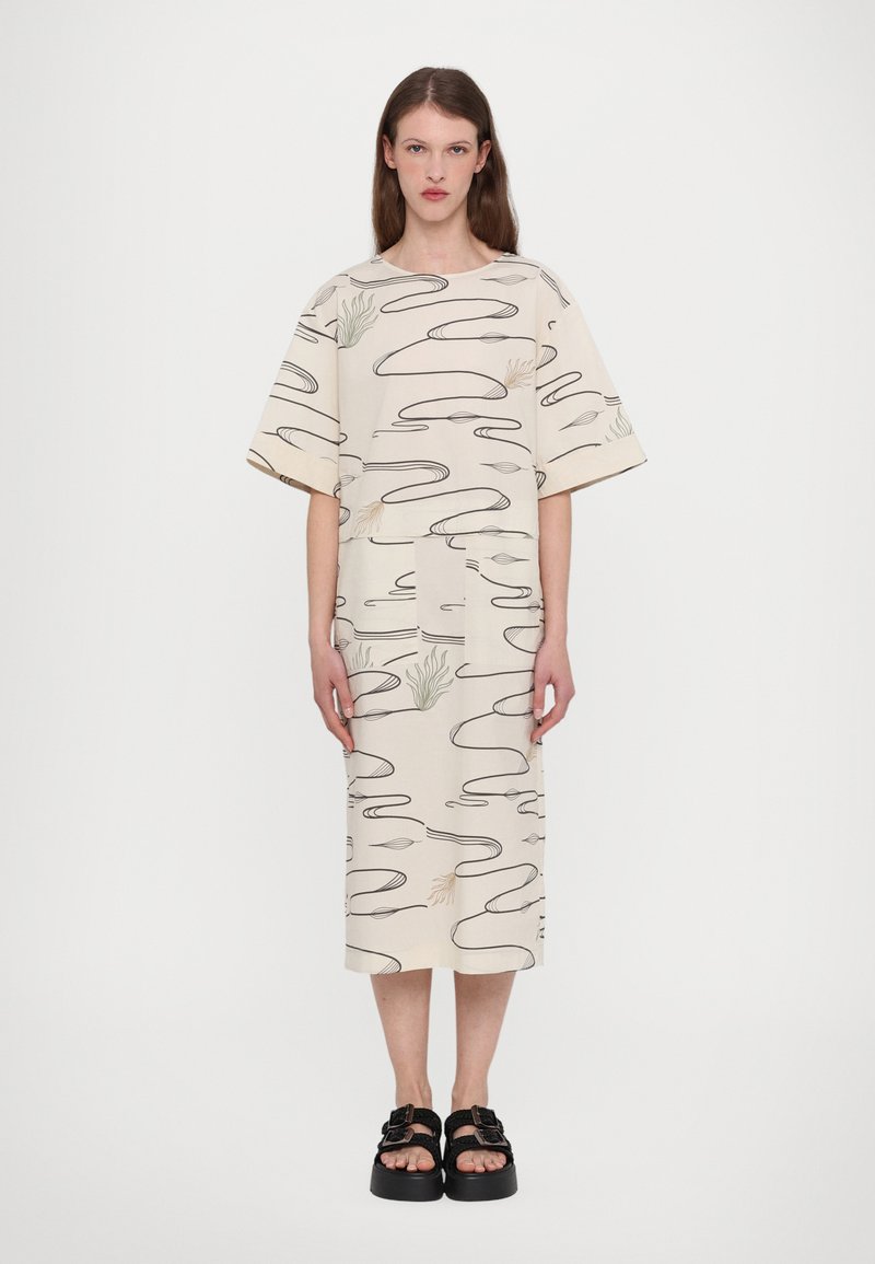 Beige mønstrete kjole med korte, brede ermer og rett snitt. Svarte abstrakte linjer og subtile plantemotiver. Kombinert med chunky svarte sandaler.
