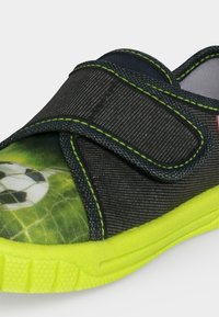Basket foncée pour enfant avec semelle jaune fluo, motif de ballon de football sur la pointe et fermeture à scratch noire avec couture verte.