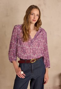 Button-up blouse with a pink and white floral pattern, soft fabric, relaxed fit, and long puffed sleeves; paired with dark denim jeans and a brown belt.