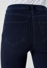 Jeans en denim bleu foncé avec une coupe slim, dotés de deux poches arrière et d'une taille mi-haute, texture lisse avec des coutures visibles minimales.