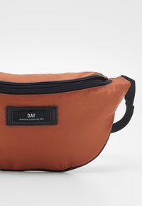 Pomarańczowa torebka na pasek z nylonu, z zamkiem błyskawicznym na górze, czarnymi akcentami i etykietą z napisem "DAY" od Birger et Mikkelsen. Kompaktowy i zaokrąglony design.