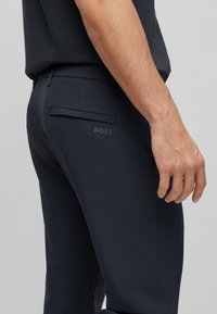 Navy trousers featuring a sleek design, made of smooth fabric, with a back pocket and a subtle BOSS logo printed in dark gray.