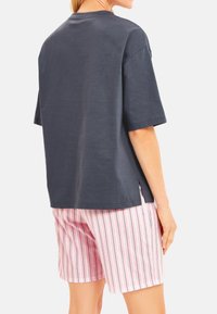Donkergrijze t-shirt met korte mouwen en een relaxte pasvorm, gecombineerd met roze gestreepte shorts met verticale marineblauwe lijnen en zijslits.