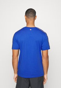 Modré tričko s krátkým rukávem a kulatým výstřihem, s černobílými pruhovanými detaily na ramenou a malým logem na zádech.