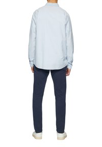 Hellblau karierte Button-up-Bluse mit langen Ärmeln, lockere Passform, kombiniert mit navyblauen Hosen und weißen Sneakern. Lässige Rückansicht.