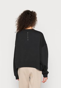 Black sweatshirt with a relaxed fit, drop shoulders, and a ribbed hem. Features vertical "NIK*E" lettering on the back. Soft fabric texture.