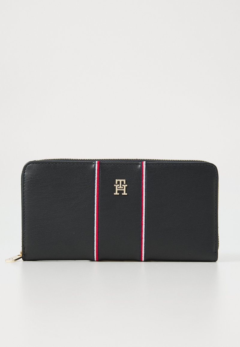 Black leather wallet features red and white stripes, gold logo accent, and zip closure. Smooth texture with sleek rectangular shape.