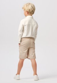 Chemise blanche à manches longues assortie à un short beige. La chemise possède un col boutonné ; le short dispose de poches avant et arrière. Baskets blanches.