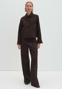 Bruine cropped jas met knoopsluiting en zijzakken, gecombineerd met brede bijpassende broek, beide gemaakt van een gladde stof.