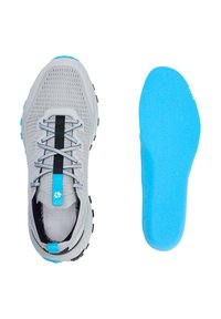 Chaussure de sport grise et noire avec des accents bleus à côté d'une semelle intérieure en mousse bleue séparée sur fond blanc.