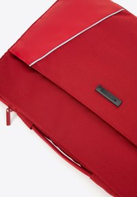 Funda de portátil sintética roja con un acabado texturizado, que presenta un acento blanco a lo largo de la abertura y una etiqueta de marca negra cosida en el frontal.