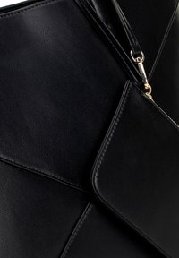 Bolso de mano de cuero negro con una textura suave. Presenta un cierre de cremallera y un bolsillo externo con solapa, que exhibe elementos de diseño angulares.