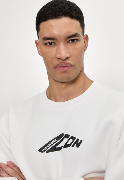 Sweatshirt blanc avec un logo graphique noir sur la poitrine. Le tissu semble doux, avec un col rond et des détails côtelés.