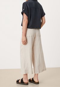 Maglietta blu navy tagliata, pantaloni in lino beige a gamba larga e sandali neri con un dettaglio intrecciato. Tessuto liscio con maniche arrotolate e dettaglio al fondo della schiena.