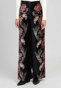 Pantalons larges noirs avec des motifs floraux paisley rouges et blancs, portés avec un haut à manches longues blanc et des bottes noires à talons pointed.