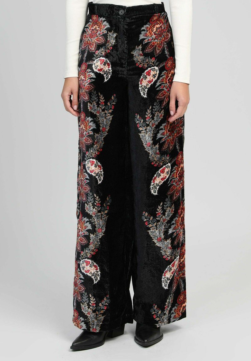 Pantalons larges noirs avec des motifs floraux paisley rouges et blancs, portés avec un haut à manches longues blanc et des bottes noires à talons pointed.